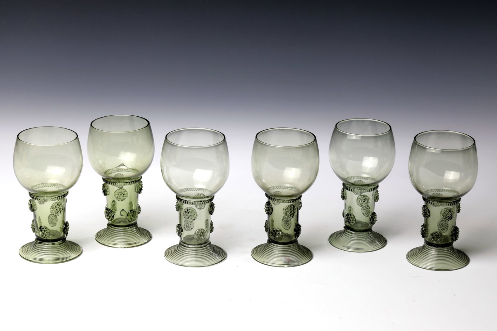 Set Six Romans: Set of six Romans German around 1800 Olive green glass with tear-off. Rising, spun foot. Shaft open at the top with two rows of offset berry nubs. Below the bulbous cuppa, a pinched thread is placed a