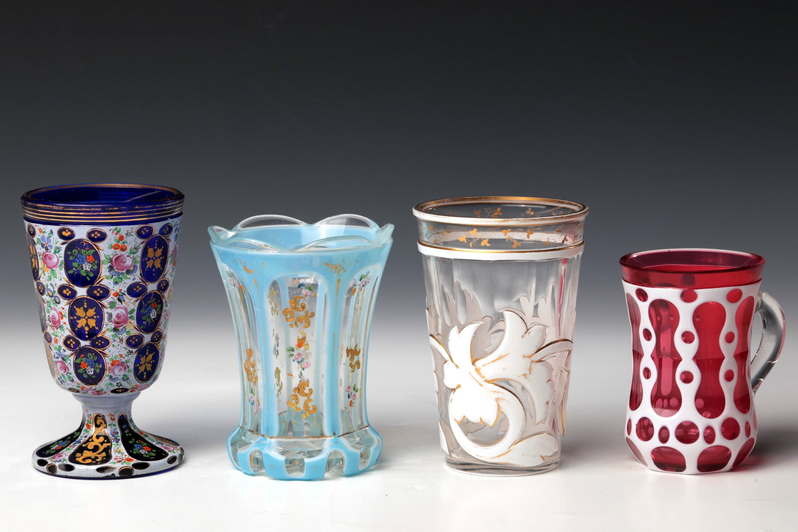 Mixed lot of four flashed glasses: Mixed lot of four flashed glasses Bohemia, 19th century Cobalt blue or colourless glass with tin enamel or light blue overlay and partly with pink underlay. Rich cut decorations and floral,