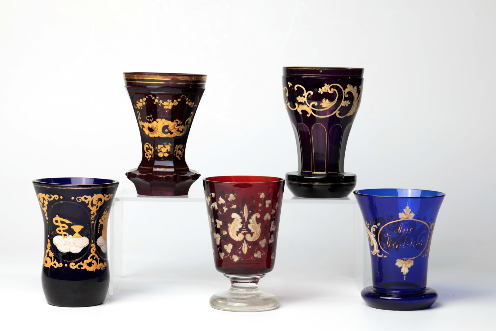Mixed lot of five Biedermeier glasses: Mixed lot of five Biedermeier glasses, 2nd half of the 18th century, colourless, varnished in different colours with enamel painting, partly heightened with gold and inscriptions. H. 11 - 13.5 cm