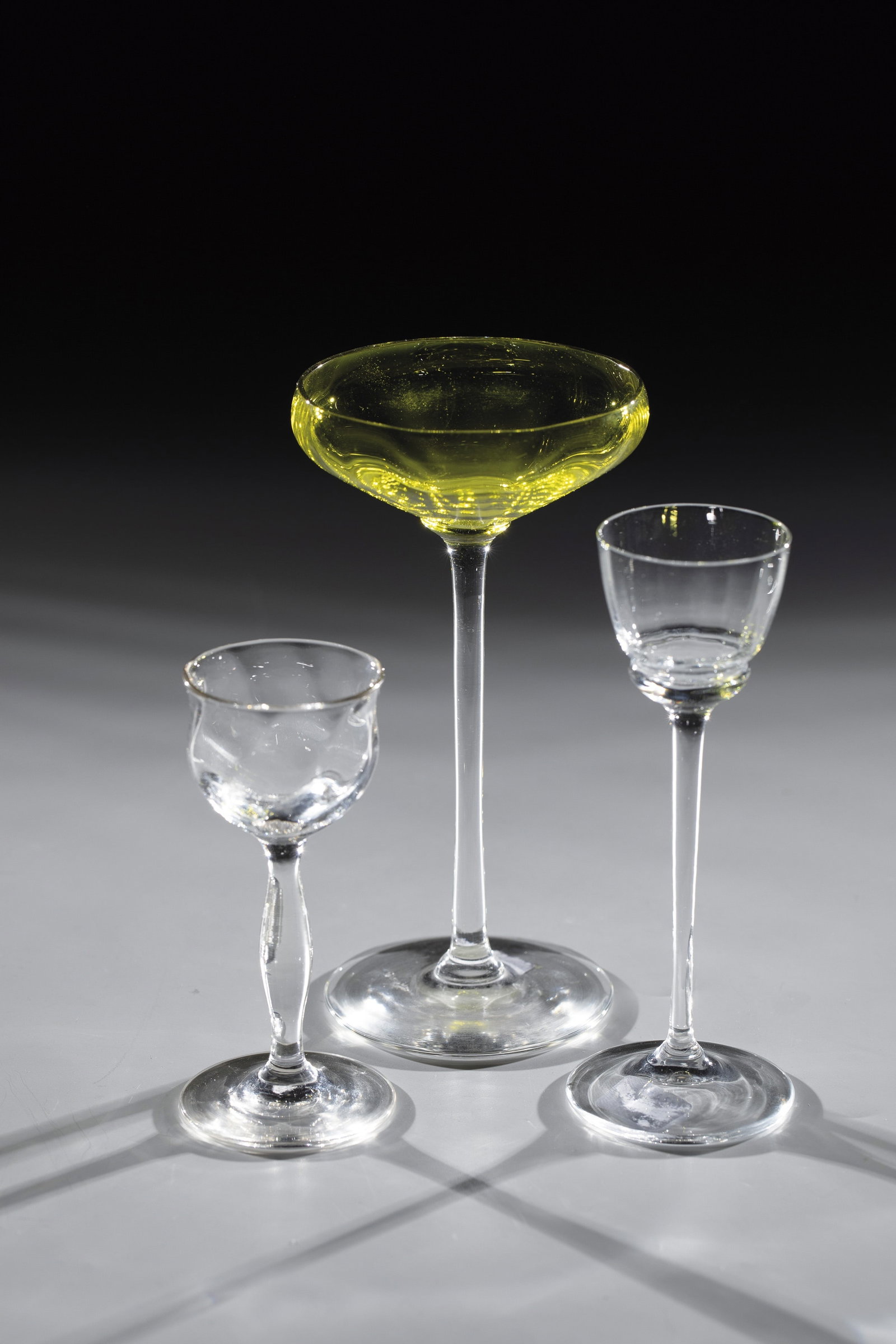 Five Liqueur Glasses: Five liqueur glasses Bohemia, c. 1910/20 Colourless or green, optically blown glass. H. 10 - 14.5 cm. Colourless glass. Shaft partially faceted and a nodus made of red glass. Both domes with repeated