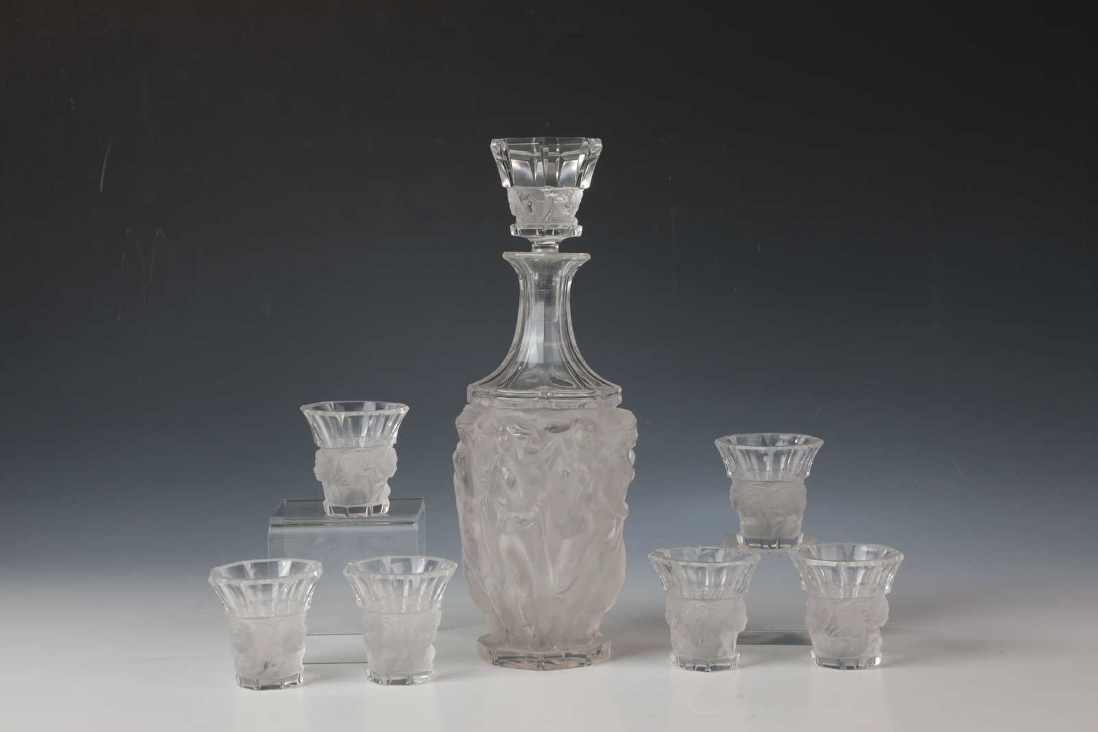 Liqueur service with semi-nudes: Liqueur service with half-nudes Wohl France, around 1930 Colourless glass. Bottle with relief decoration surrounding the wall: dancing, antique-style female figures in flowing robes and long hair, mat