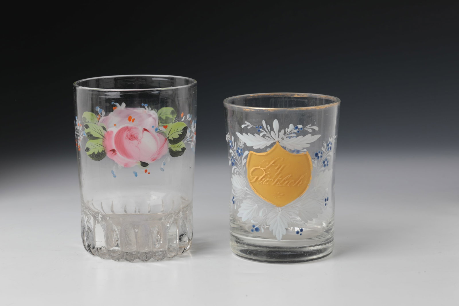Two cups: Two Black Forest goblets, 19th century Colourless, partly modelled glass with polychrome enamel painting and inscription ''Sey Glücklich'' in gold. H. 10.5 or 11.5 cm Zwei Becher Schwarzwald,