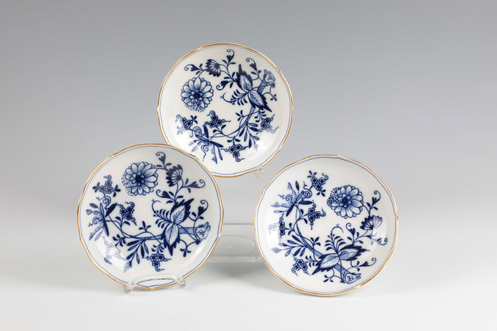 Three bowls: Three bowls Meissen, 20th century Round, flat arched shape on a standing ring with a passing, gilded edge. Underglaze blue décor: onion pattern. Underglaze blue sword mark and in black monogram
