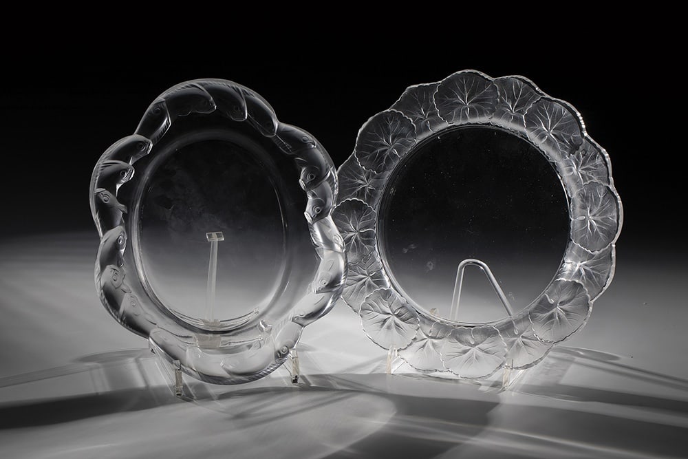 Two plates: Two plates of Lalique, Wingen-sur-Moder, 20th century Colourless glass, pressed into the mould, partially finished by polishing. Relief decoration on the flags: frieze with fish or leaves. Underside
