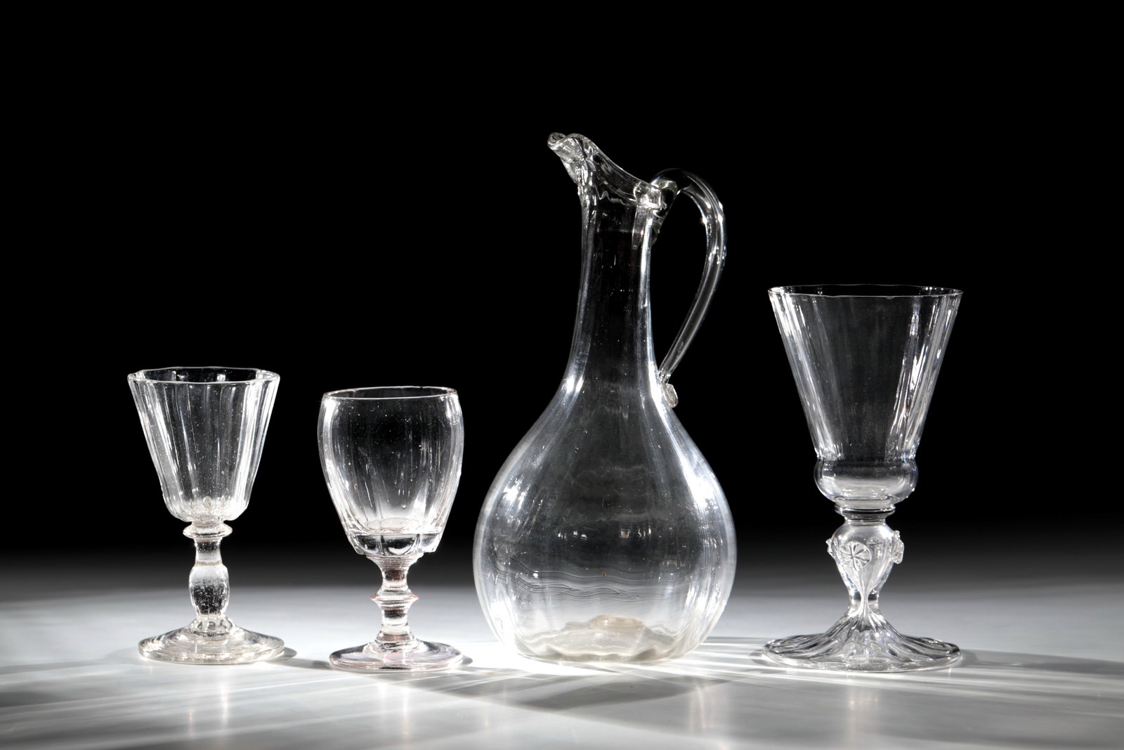 Mixed lot of three glasses and a gift jug: Mixed lot of three glasses and a gift jug France, E. 18th century Colourless, longitudinally optically blown glass with tear-off and downturned muzzle rim. Spout pinched. Appliquéd handle with