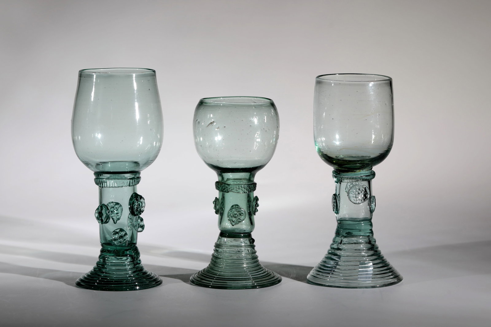 Three Romans: Three Romans German, 19th century Light green glass with tear-off, ribbed trumpet base, hollow shaft with applied berry nubs. At the base of the bulbous cuppa, a thread pinched all around. H. 15.5 or