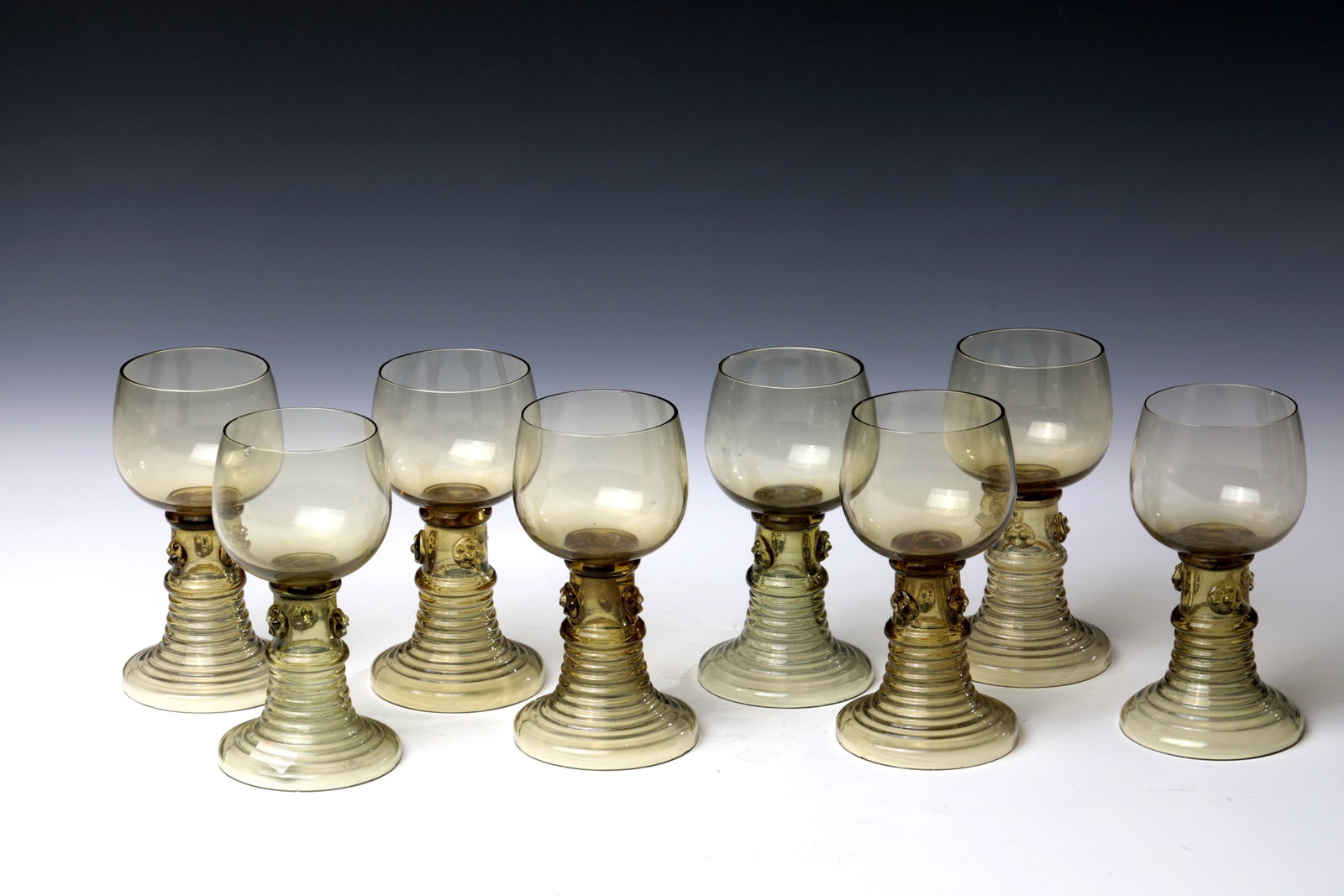 Eight Romans: Eight Romans German 19th century Olive-green glass with raised, ribbed trumpet base. On the hollow shaft three applied berry nubs. Partly bumped. H. 13 cm each. Acht Römer Deutsch 19. Jh. Olivgr&