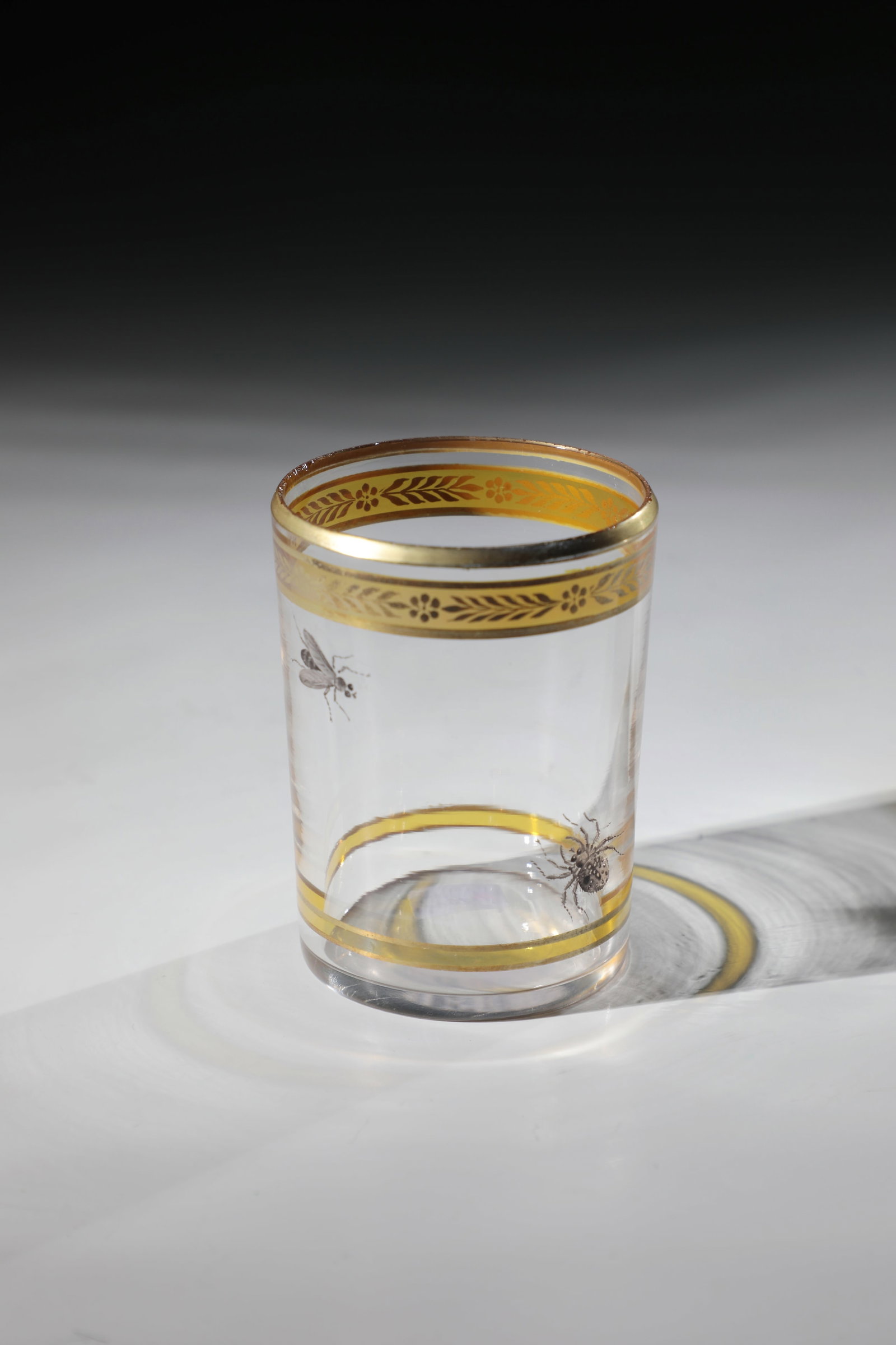 Cylinder cup: Cylinder cup Germany or Bohemia, 1st half of the 19th century Colourless glass. On the cylindrical wall between two yellow-stained borders, a spider and a fly in black solder painting. Gold-plated