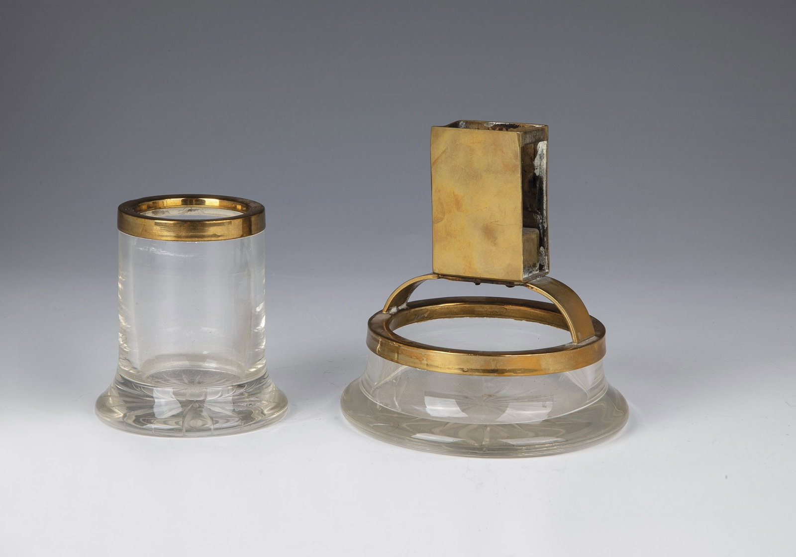 Two-Piece Cigar Set: Two-piece cigar set 20th century Colorless glass with cut star in the bottom. Brass mount. Dents. H. 8 or 12.5 cm. Zweiteiliges Zigarrenset 20. Jahrhundert Farbloses Glas mit Schliffstern im Boden.