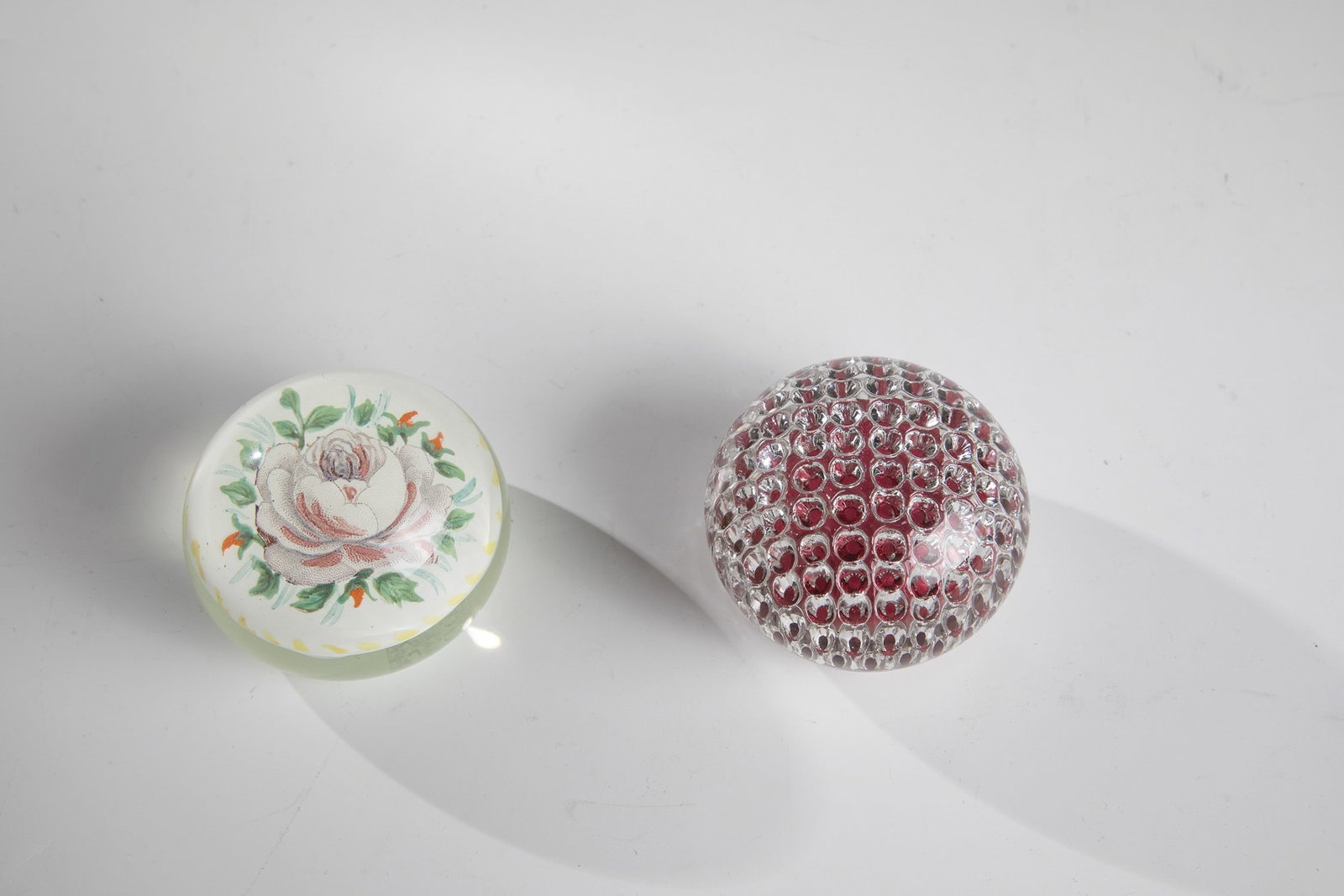 Two paperweights: Two paperweights France, 20th century A paperweight made of colourless glass with red cushions and honeycomb decoration and a paperweight with a drawing of a rose captured in glass. D.7.2-7.3cm H.5.2-