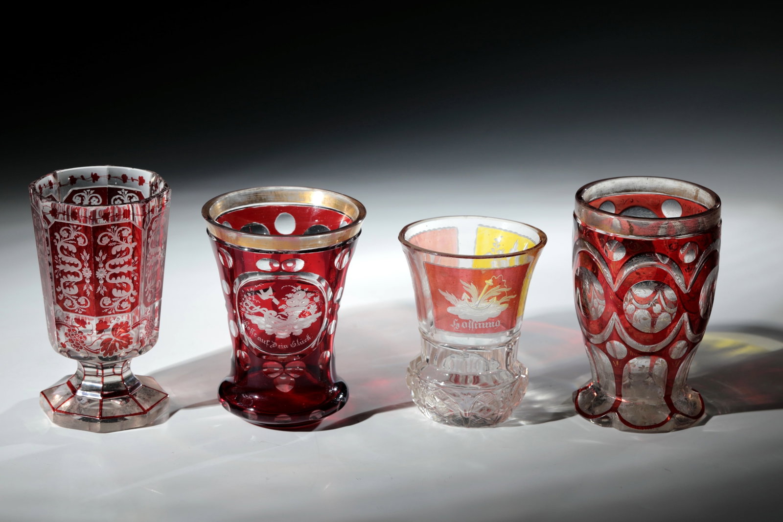 Mixed lot of four coloured glasses: Mixed lot of four coloured glasses Bohemia, 19th century Colourless glass with red and partly yellow glaze, rich shield decoration and allegorical depictions in fine engraving: Hope, Faith, Happiness