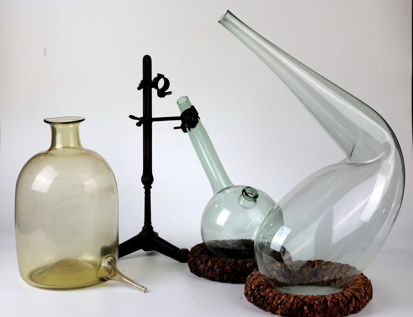 Bundle of three laboratory vessels and a tripod: Mixed lot of three laboratory vessels and a tripod 19th century Consisting of a alembic with iron stand, a retort and a still with bottom outlet. Light green or honey-yellow glass. H. 38 to 44 cm