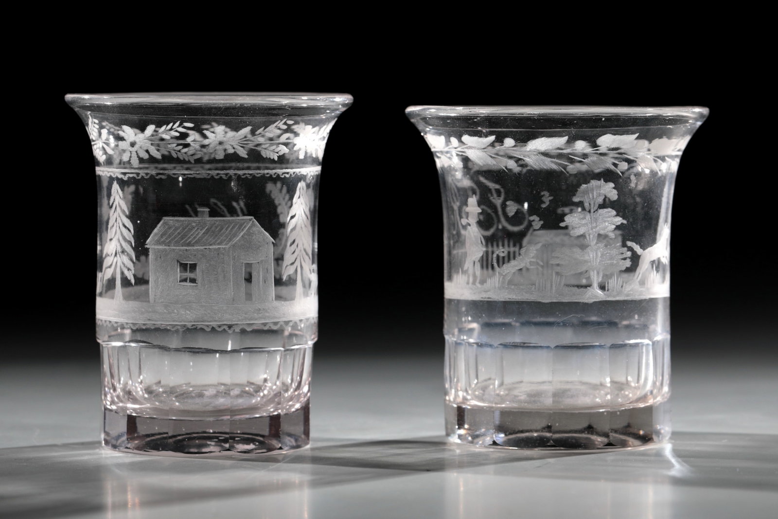 Two Empire Mugs: Two Empire Goblets, circa 1820, Colorless glass. Slightly hollow sanded bottom. The approach of the protruding wall is faceted. On the wall cut depiction of a hunter with a dog in tree-lined