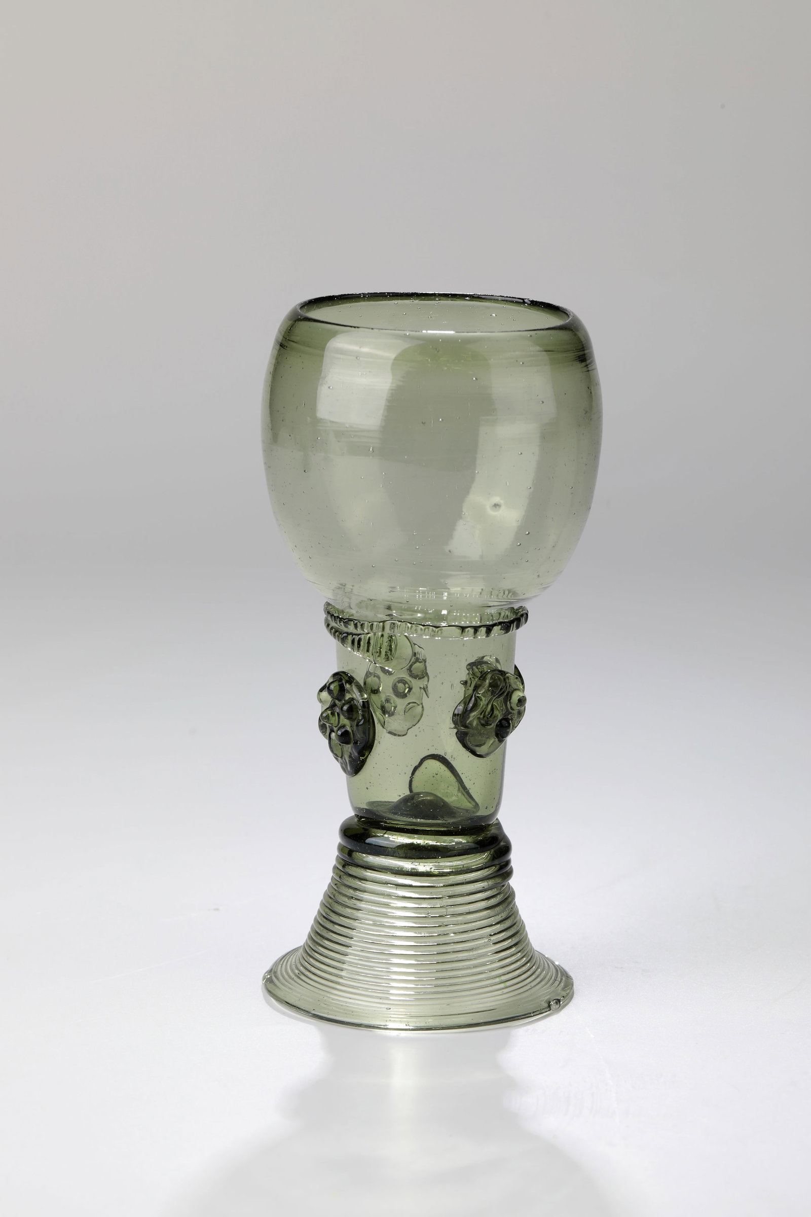 Romans: Roman, German, 18th century, olive-green glass with tear. Spun foot. Shaft open at the top with appliquéd berry nubs. Below the bulbous cuppa, pinched thread damaged. H. 13 cm