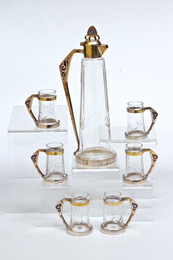 Siebenteiliges Wodkaset: Siebenteiliges Wodkaset Russland, um 1900 A seven-piece metal-mounted colourless glass vodka set comprising a decanter and six beakers. The handles decorated with blue enamel. Marked with firm's mark 