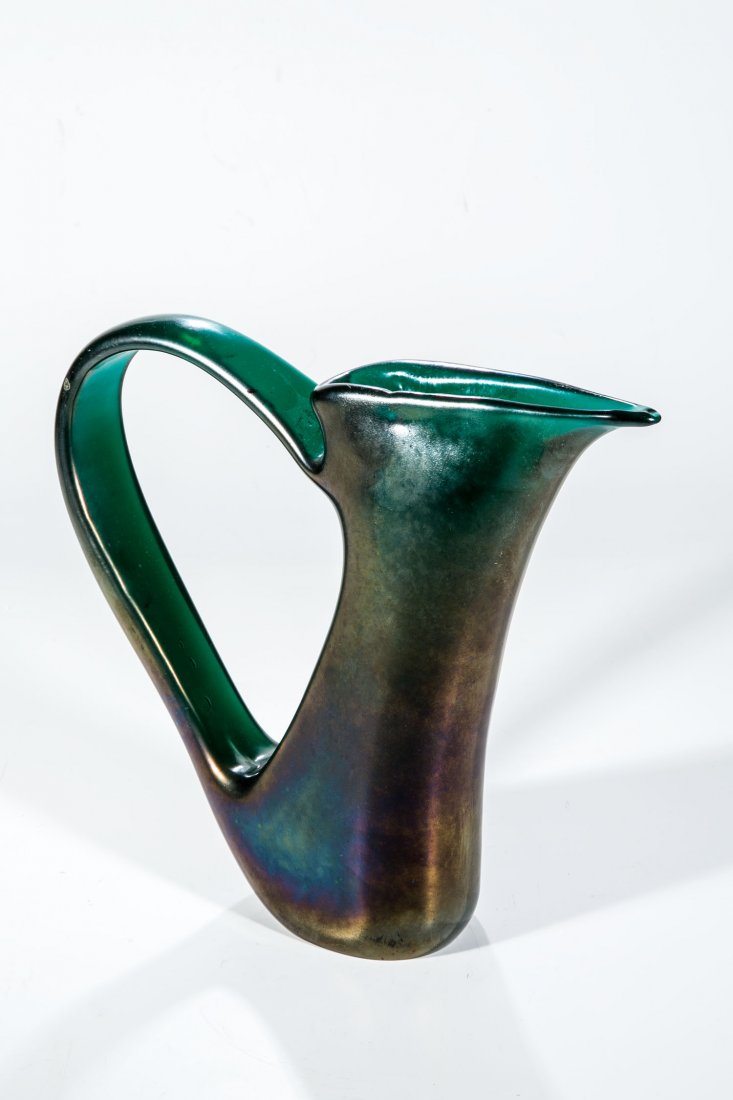 Henkelvase ''Ad Ansa Volante'': Henkelvase ''Ad Ansa Volante'' Giorgio Ferro (Entwurf), AVEM, Murano, 1952 Dunkelgrünes Glas. Weit ausschwingender Bandhenkel aus der Wandung gezogen. Irisiert. H. 24,5 cm Lit.: M. Barovier, Il Vetro