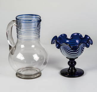 Henkelkrug und kobaltblaue Fußschale: Henkelkrug und kobaltblaue Fußschale Thüringen und Weserbergland, 19. Jh. Krug aus farblosem Glas mit Sandabriss und am breiten Hals aufgelegten Fäden aus blauem Glas, diese min. best., H. 23 cm.