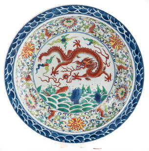 Chinese Wucai Porcelain Charger: Chinese Wucai glazed porcelain charger with painted central scene depicting a dragon chasing the flaming pearl over waves, bordered by scrolling foliate and wave decoration. Exterior of body with