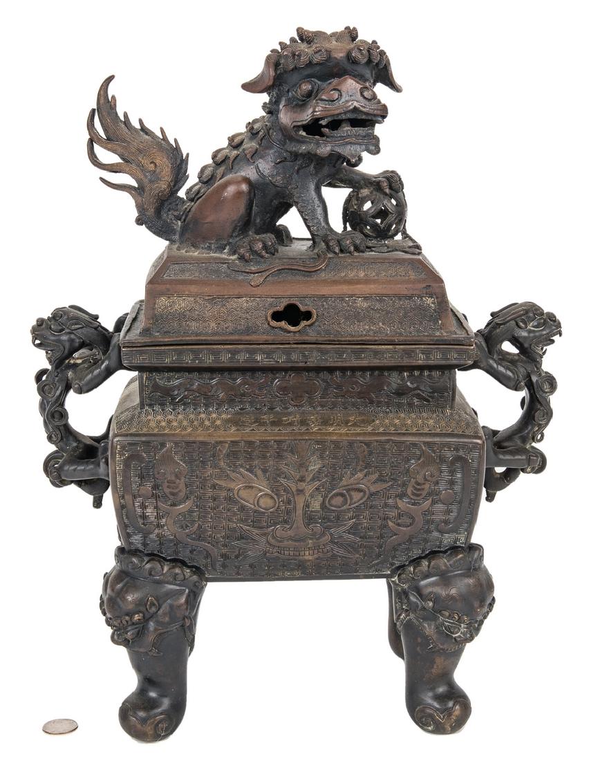 Large Chinese Bronze Foo Dog Censer: Large Chinese bronze lidded ritual censer, the top with a figural foo dog or dragon posed with its left front paw atop a pierced ball, the base with foo dog or dragon figural handles, taotie mask deco