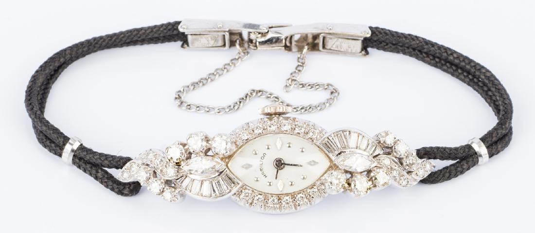 Vintage 14K Hamilton Diamond Watch: Vintage 14K white gold lady's Hamilton diamond dress watch face with black cord strap. Oval watch top designed in diamond swirl pattern consisting of marquise, round and straight baguette diamonds wit