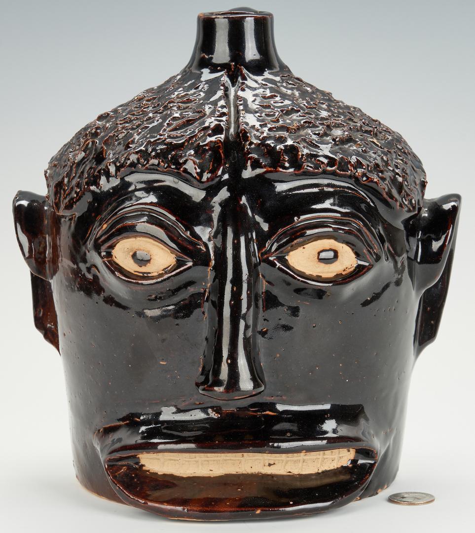 Folk Art KY Face Vessel, Ernest Galloway: Kentucky folk art stoneware pottery face vessel having an Albany slip glaze with curly hair parted in the middle, unglazed eyes and open mouth with scored teeth. Small unglazed circles in the center o