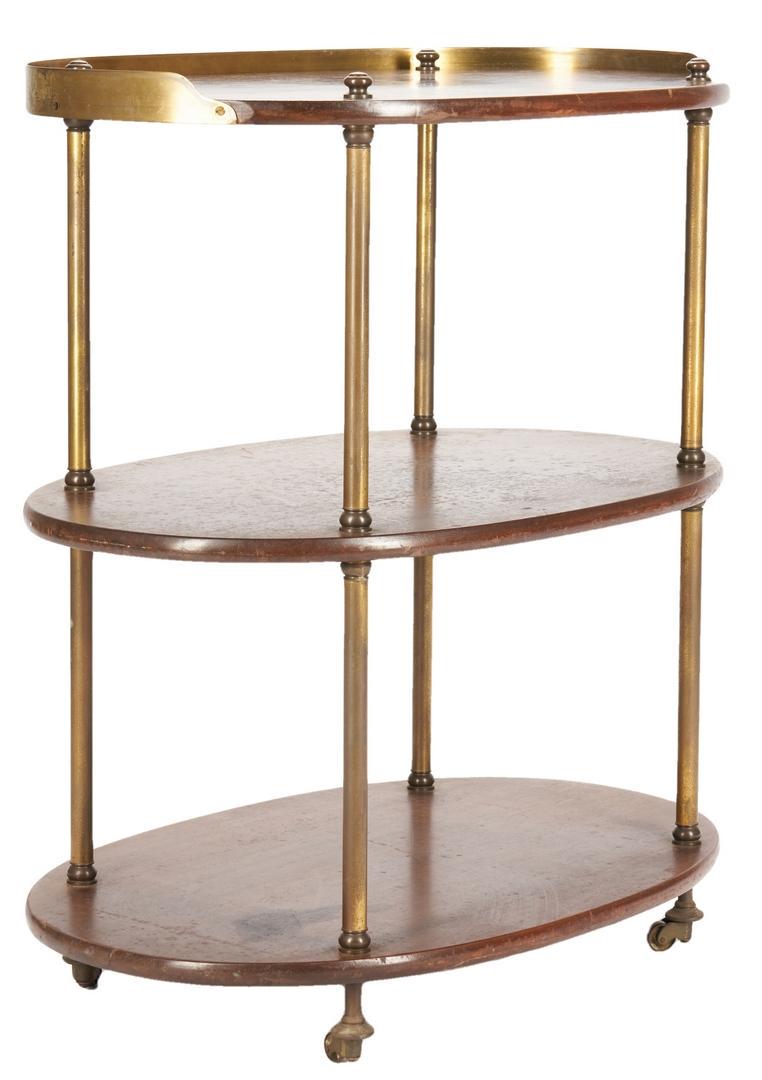 Three tiered wood and brass bar cart: Three-tiered brass-mounted mahogany rolling bar cart, oval form with partial brass gallery to top tier, two lower tiers joined by brass posts, atop four casters. 30" H x 26 1/2" W x 17 1/2" D. America