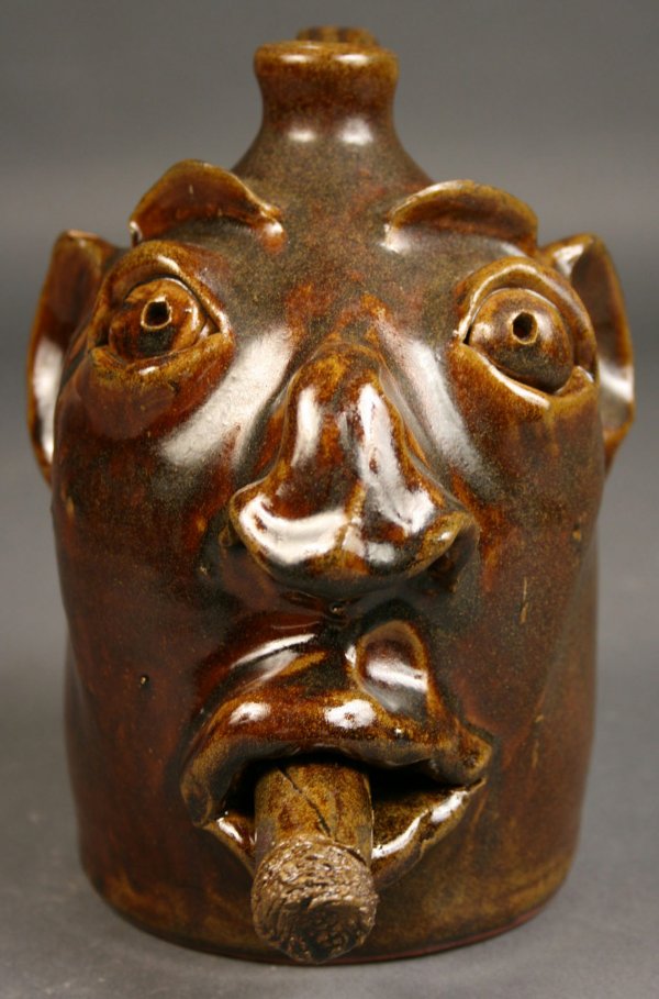 Robert Brown folk pottery face jug: Brown pottery face jug with cigar in mouth. Brown glaze. Marked on bottom "Brown's Pottery Robert Brown". Excellent condition with an unglazed mark on the ear, probably from kiln stacking. 7 1/2" heig