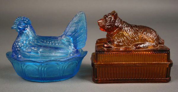 Amber and Blue glass covered boxes of animals: Lot of two items. 1 st item - Amber glass covered dish with dog. Small chip to corner of lid and inside lip of lid. 4 3/8" height (with lid) x 4 7/8" length x 3" depth. 2nd item - Blue glass chicken d