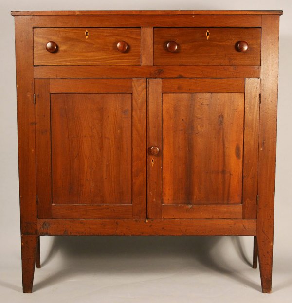 Middle Tennessee cherry press: Middle TN cherry press, with walnut secondary. Consisting of two dovetailed drawers with wooden pulls and inlaid escutcheons over two mortised doors on tapered legs. Interior fitted with one shelf. Co