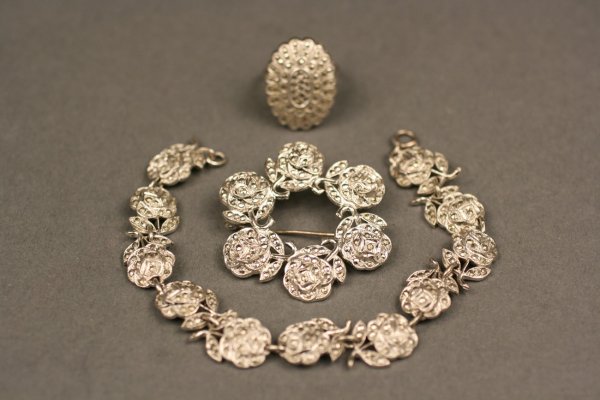 Three marcasite jewelry items: Lot of three items. 1st item - Silver and marcasite brooch with six roses, in circle design. Marked "STERLING" 1 3/4" diameter. .395 oz troy. 2nd item - Silver and marcasite bracelet with eleven rose 