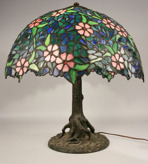 Art Nouveau table lamp: Art Nouveau leaded glass table lamp, domed shade having floral and leaf decoration in shades of blue, green and pink marked "Handel" with tree trunk bronzed base impressed "Handel". Lamp was most like
