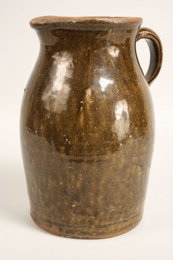 Georgia alkaline glaze stoneware pitcher: Georgia alkaline glaze stoneware pottery pitcher in brown drip design. Very good condition with old minor exfoliation to rim and noted scattered firing imperfections. Measures 10 1/4" H x 6" base. 19t