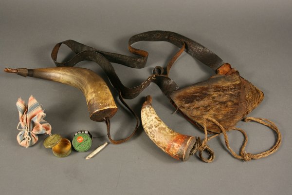 Leather hunting bag with frontier items : Leather hunting bag with powder horns, percussion cap containers and lead musket balls. 1st item - Early brown leather hunting bag with triangular flap and strap. Remnants of fur to front of bag. Very