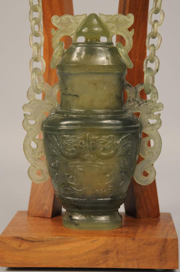 Asian Green Jade Hanging Chain Vase: Chinese sage green jade hanging chain vase with wooden display. Carved detail to chain & vase. Separate lid to vase. Jade vase - 10 5/8" Height x 4 1/8" Width. Vase & stand - 11 5/8" Height.