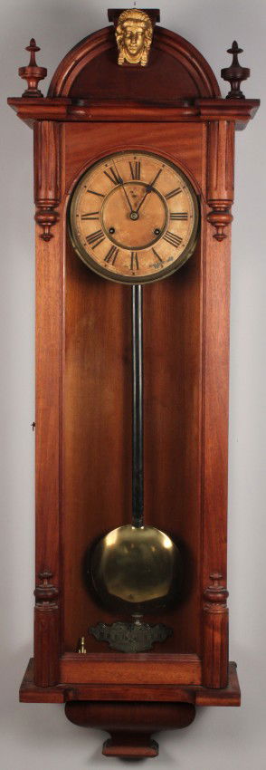 Ansonia Regulator No. 4 Clock, late 19th century: Ansonia "Capitol" model Regulator wall clock. Spring driven movement. Oak case with arched crown and upper finials, applied gilt metal "Liberty" mask, single long door with applied detail and a molded