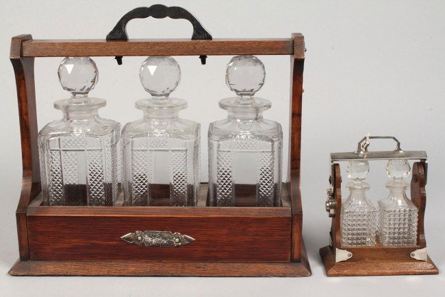 2 Glass Tantalus Sets, one miniature: Lot of 2 Edwardian Oak and Glass Tantalus Sets, both with keys. 1ST ITEM: Tantalus set with three pressed glass bottles, very good condition, 13 1/4" H x 15" W x 5 3/4" D. 2ND ITEM: Miniature Tantalus