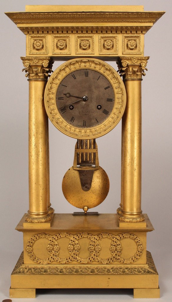 French Empire Portico clock: Neoclassical style gilt bronze clock, architectural flat molded cornice with a band of rosettes across the frieze, supported by Roman Corinthian columns. Round face suspended above a plinth with appli