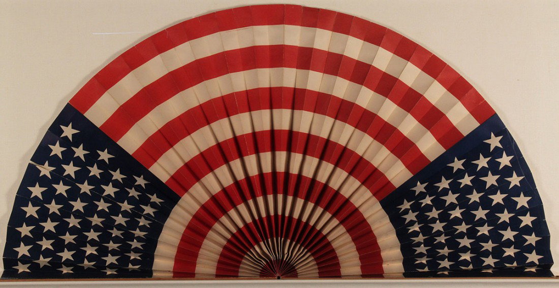 Cased Pleated Paper Parade Flag, Semicircular: Large framed flag parade flag, pleated in a semicircular fan, containing 45 stars and manufactured by the "Deutz Litho Co Makers, 78 Beekman St., NY". Housed in plexi-glass case. 23 1/4" H x 45 1/4" W