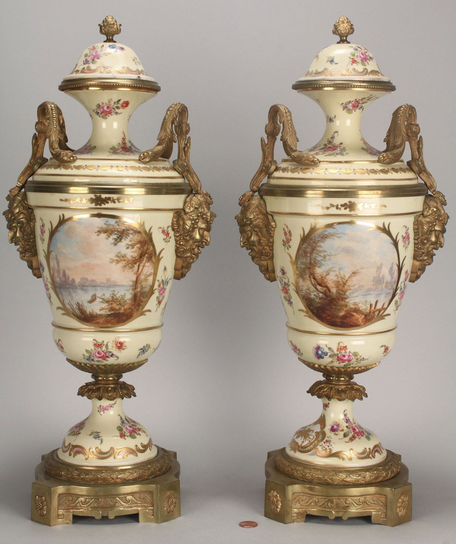 Pair of Sevres Ormolu Urns, 19th century: Pair of Sevres Ormolu Covered Urns, with twin handles and hand-painted cartouches of Watteau-like lovers on one side and waterscapes on the other, with scattered floral sprays and gilt decoration. Sev