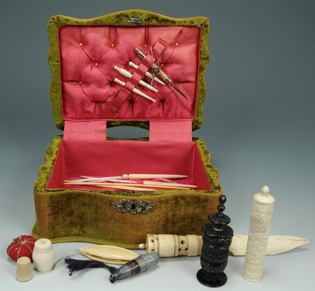 Lot of 22 ivory sewing notions in velvet box: A green velvet covered serpentine shaped sewing box with silver mounts and handle and tufted fuscia silk lining, containing 22 ivory sewing implements and a red fabric pincushion. Sewing notions inclu