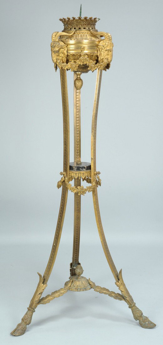 Neoclassical style torchiere or pricket stand, 47": Neoclassical style gilt brass or bronze floor torchiere, candle pricket stand with three figural ram heads joined by floral swags, supported on three feet ending in hoof feet and joined by a black ony