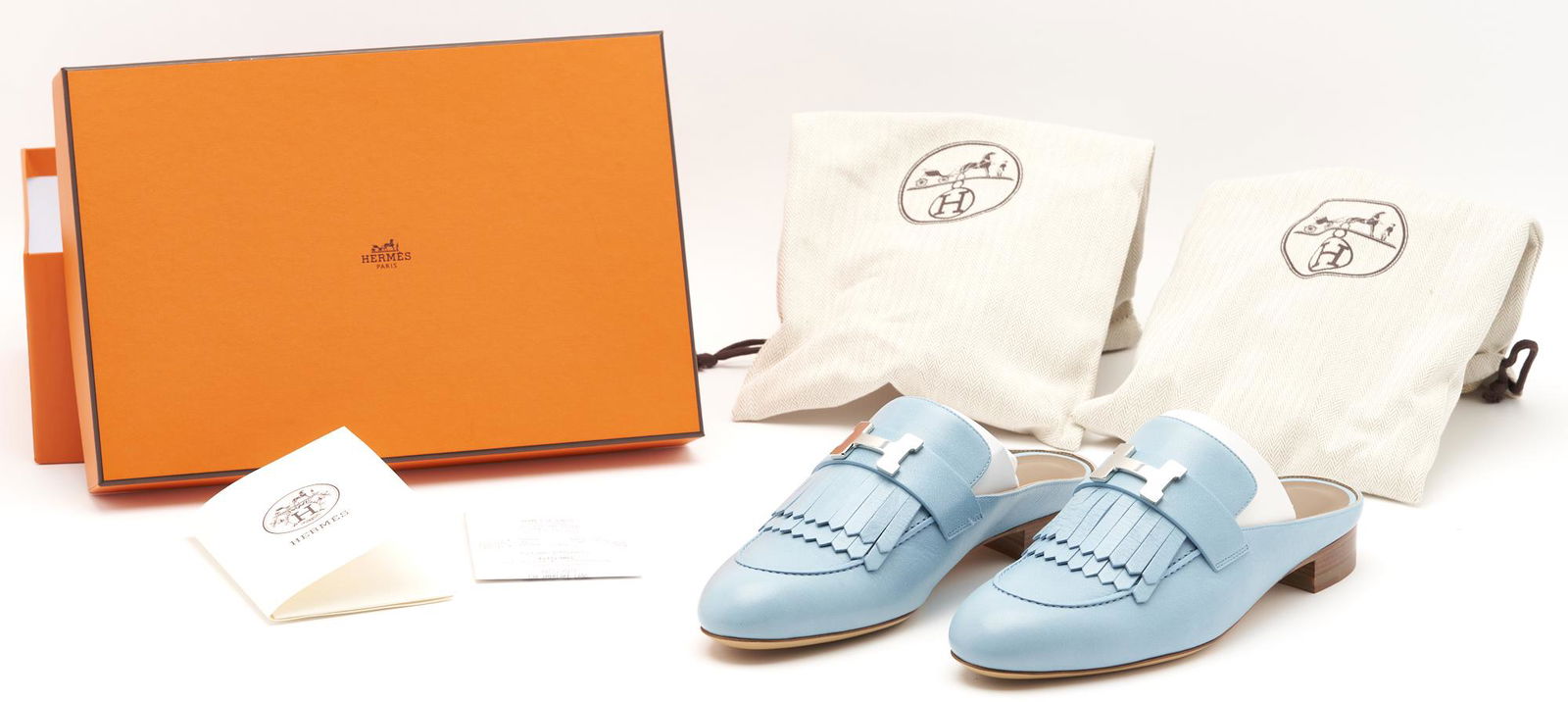 Hermes Rivoli Bleu Ciel Calfskin Mules: Pair of Hermes "Rivoli" Bleu Ciel calfskin mules with fringe detail, palladium-plated signature "H" faux buckle, and goatskin lining. Labeled "Hermes" to insole and sole; serial number embosed to lini