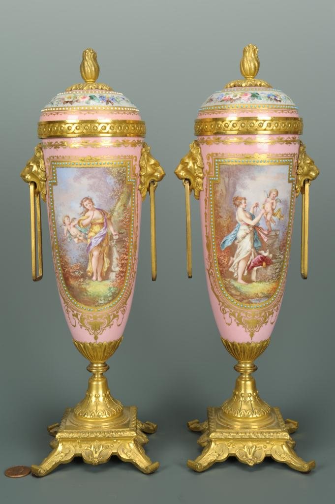 Pr. of French Gilt Bronze Mounted Porcelain Urns: Pair of French gilt bronze mounted Sevres style porcelain covered urns, each with floral and figural hand painted and gilded decoration, on a pink ground with romantic women and cherub vignettes . Lio