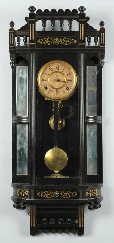 Ansonia Reflector Wall Clock in Ebonized Case: Ansonia "Reflector" hanging wall clock, ebonized Eastlake style case with a gilt-decorated spindled gallery top, mirrored side shelves, clear glass door and a small, gilt-stenciled drawer. Retains int