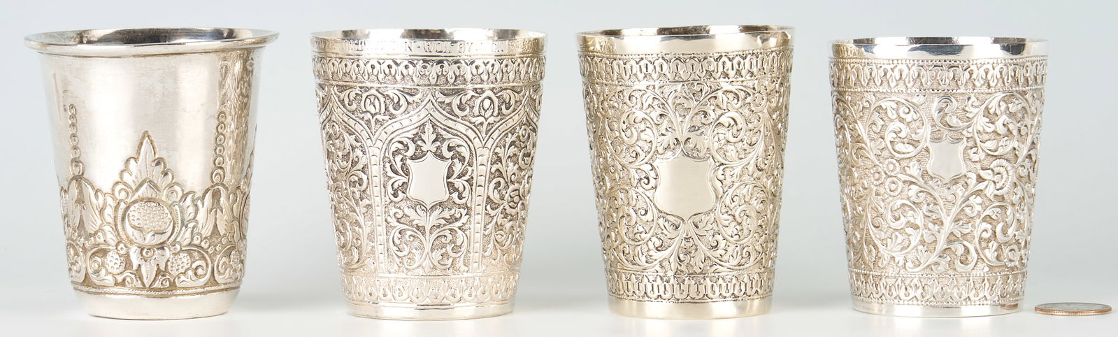 4 Asian silver cups including Rifle Presentation Trophy Cup: Four (4) Asian silver cups or beakers. Three (3) of similar but not identical design, each with overall repousse scrolling and floral motif and shield cartouche. One with trophy inscription to rim: "Q
