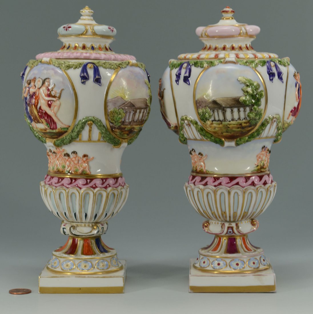 Pair of Covered Capo di Monte Porcelain Urns: Pair of covered Neoclassical style porcelain urns with classical figural and landscape relief decoration and blue Capodimonte mark to the bases. 9 1/2" H. 19th century. Provenance: A Mississippi