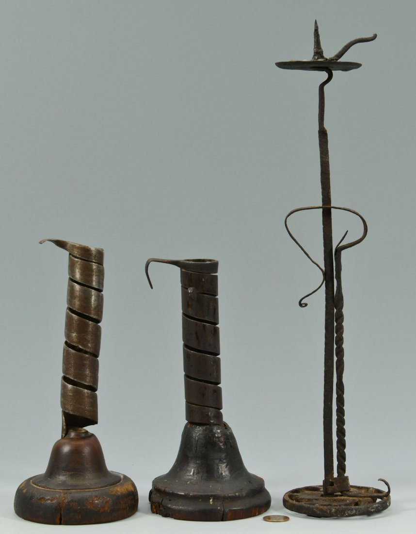 Three 18th century lighting devices: Grouping of three 18th century lighting devices including 2 early iron spiral candlesticks with wooden bases and 1 iron candlestick with a spiral column and adjustable trammel, tulip foliate design in