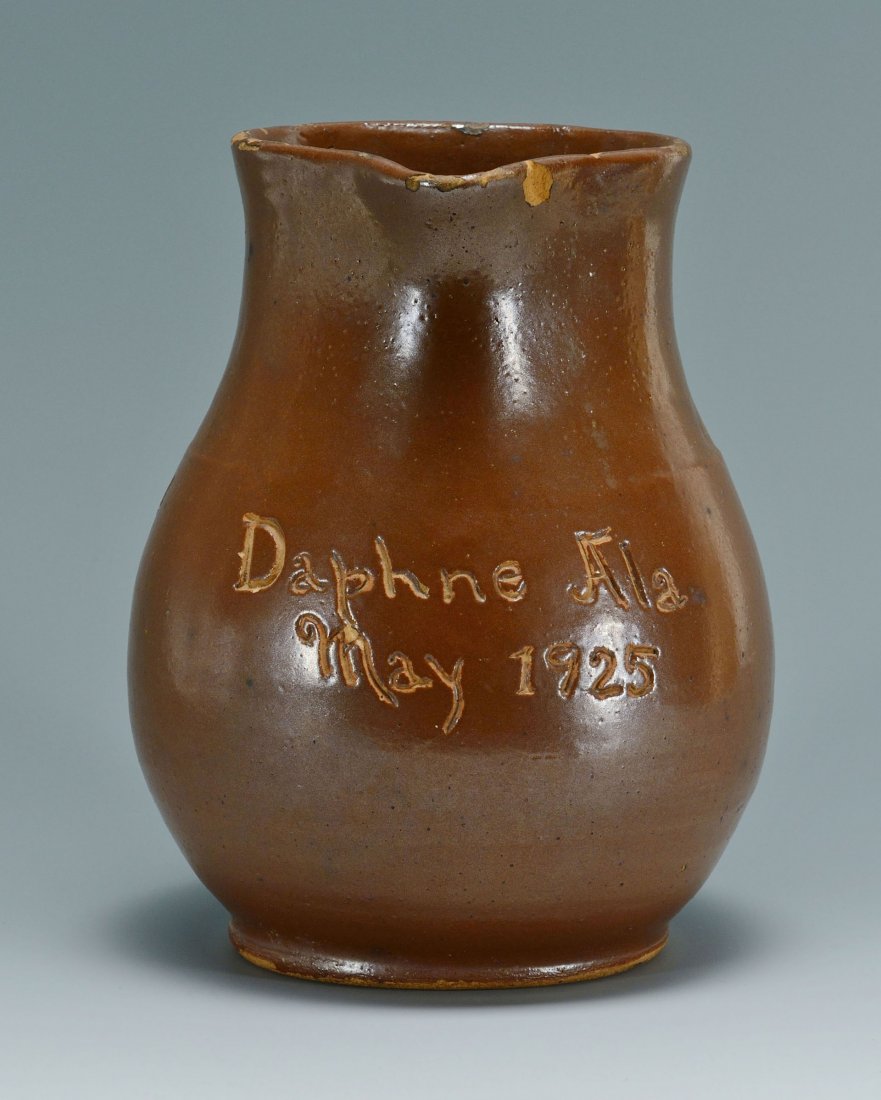 Alabama Redware Pottery Pitcher: Alabama redware pottery pitcher inscribed "Daphne, Ala May, 1925". Having an all over red slip glaze and an unusual pulled and applied rattail design handle. 8 1/2" H. 1st quarter 20th