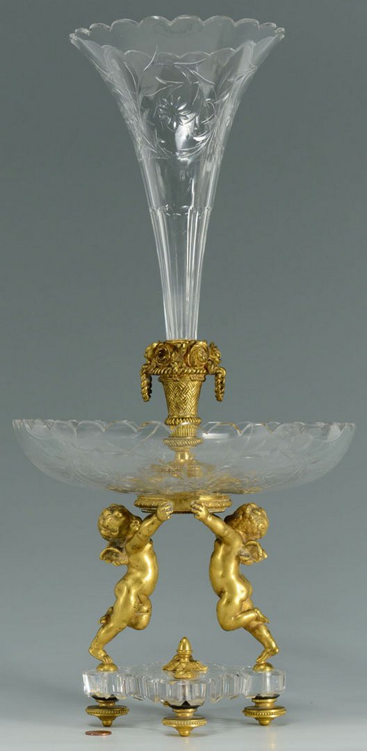 Baccarat Crystal & Gilt Bronze Figural Epergne: A Baccarat etched crystal and gilt bronze figural epergne featuring two standing cherubs supporting a crystal bowl with a central trumpet vase. Marked Baccarat on the bronze base of the trumpet vase. 