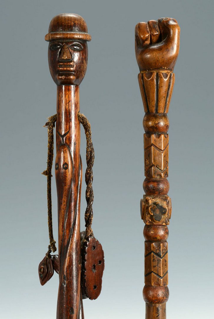 2 Folk Art Carved Figural Canes, poss. Native American : 2 Folk Art carved figural canes. 1st item - Carved folk art cane depicting a man with top hat, probably Native American, having a snake carved shaft with black dot decoration. Twisted leather through